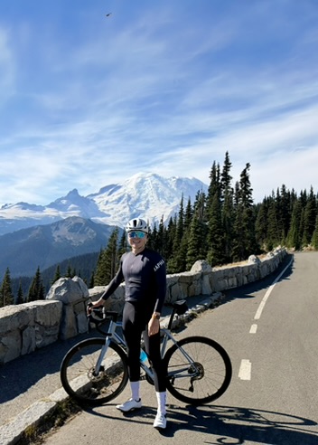 Ryan with his road bike on a mountain road, snow-capped peak behind